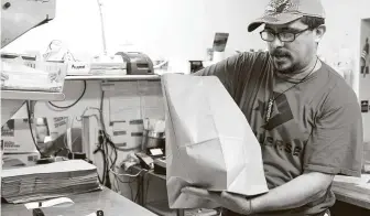  ?? Gustavo Huerta / Staff photograph­er ?? A worker at Mel’s Country Café in Tomball bags meals for curbside pickup.