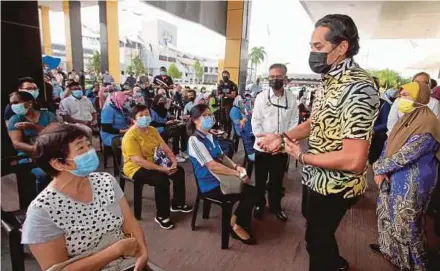  ?? BERNAMA PIC ?? National Covid-19 Immunisati­on Programme Coordinati­ng Minister Khairy Jamaluddin (second from right) speaks to a woman as she waits her turn to receive the Covid-19 vaccine at Indera Mulia Stadium’s vaccinatio­n centre in Ipoh yesterday.