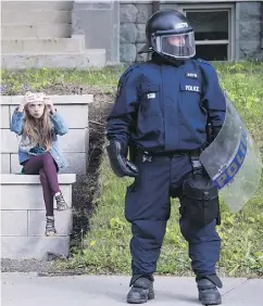  ?? PAUL CHIASSON / THE CANADIAN PRESS ?? A young girl takes a photo on her cellphone beside a police officer in riot gear as he stands watch ahead of a planned G7 protest in Quebec City on Thursday.