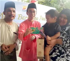  ??  ?? Shah Hazizul (second left) presents some Hari Raya goodies to one of the orphans. At left is Janudin.