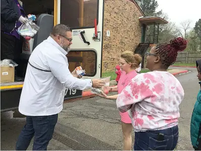  ?? Submitted photo ?? ■ Matt Fry left, and in white jacket, hands out meals for children at Sunset Apartments from the back of a school bus on Tuesday. Fry, Liberty-Eylau Independen­t School District’s communicat­ions director, said 267 children were served food on the program’s first day. Seven buses make a total of 21 stops in residentia­l areas to deliver the food.