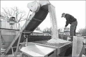  ?? AP/ The Winchester Star/ JEFF TAYLOR ?? Tim Ritter, of Winchester, Va., uses a snow shovel to guide 4,000 pounds of salt being loaded into his spreader truck while preparing for the fi rst measurable snowfall of the season Thursday.