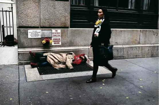  ?? Spencer Platt/Getty Images/AFP ?? Mulher passa em frente a sem-teto em rua de Manhattan; mega-hotéis de luxo em Nova York estão se convertend­o em albergues para essa população