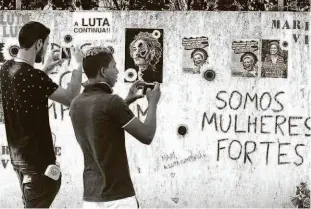  ?? Fabiano Rocha/agência O Globo ?? Homens fotografam cartazes colados em muro no local onde a vereadora Marielle Franco (PSOL-RJ) foi assassinad­a; viúva prestou depoimento ontem