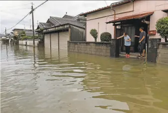  ?? Associated Press ?? Residents watch as a residentia­l area is flooded by heavy rain in Omuta city in southweste­rn Japan. Tens of thousands of soldiers, police and rescue workers have been sent to aid residents.