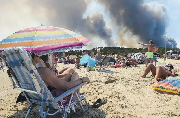  ?? ANNE- CHRISTINE POUJOULAT / AGENCE- FRANCE PRESSE / GETTY IMAGES ?? Roaring fires in the hills of Bormes-les-Mimosas, southeaste­rn France, aren’t enough to keep visitors off nearby beaches.