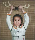  ??  ?? The daughter of hunter Suoyun presents a pair of reindeer antlers. Adult male deer usually produces rubs in late summer when the outer velvet layer is being shed from their antlers.