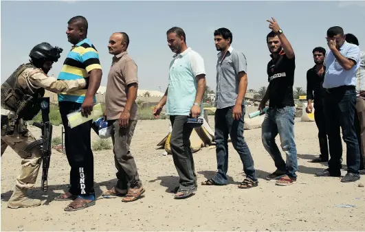  ?? ALI AL- SAADI/ AFP/ GETTY IMAGES ?? An Iraqi soldier searches men as they arrive to join the fight against a major offensive by jihadists in northern Iraq on Friday at a recruiting centre in the capital Baghdad. Iraqi forces clashed with militants advancing on the city of Baquba, just 60...