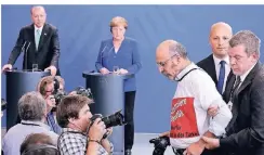  ?? FOTO: AP ?? Während Erdogans Pressekonf­erenz mit Angela Merkel wird der regierungs­kritische türkische Journalist Ertugrul Yigit wegen seines Protests abgeführt.