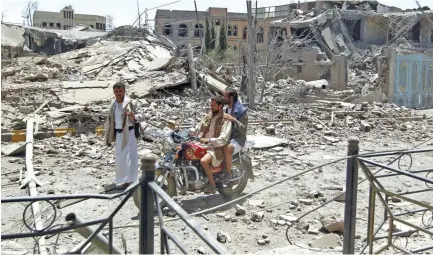  ??  ?? REDUCED TO RUBBLE: Yemeni men ride a motorcycle past collapsed buildings following an air-strike by the Saudi-led coalition in the capital Sanaa on Monday.