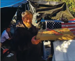  ?? COURTESY PHOTO ?? A man at a homeless encampment at Interstate 280 and Stevens Creek Boulevard holds a pizza given to him by a group of volunteers who recently donated food and blankets to homeless people in San Jose and Cupertino encampment­s.