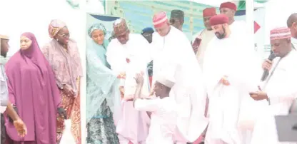  ?? PHOTO: NAN ?? Governor Abba Yusuf of Kano State (M) assisted by the Chairman, Dangote Group, Alhaji Aloko Dangote (4th L), while presenting food items to a beneficiar­y during the distributi­on of palliative­s to Kano residents by the Dangote Foundation in Kano on Saturday