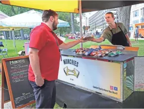  ?? MICHAEL SEARS/MILWAUKEE JOURNAL SENTINEL ?? Aidan Benkowski, one of the owners of the Munchies food cart, hands a sandwich to a customer during the Westown Farmers Market, held 10 a.m. to 2 p.m. Wednesdays through Oct. 31 at Zeidler Union Square, N. 3rd and W. Michigan streets.