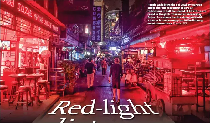  ?? Photos: AFP ?? People walk down the Soi Cowboy touristic street after the reopening of bars as restrictio­ns to halt the spread of COVID-19 are eased in Bangkok, Thailand on Wednesday. Below: A customer has his photo taken with a dancer in a near-empty bar in the Patpong entertainm­ent area.