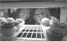  ?? STAFF PHOTO BY DARWIN WEIGEL ?? Michelle Koos and her daughter Nicole Koos pose for a picture through one of the cupcake display cases at Michelle’s Cakes in Indian Head.