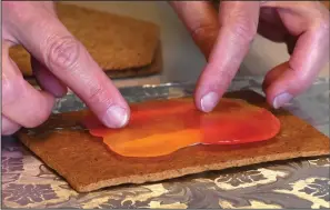  ?? ?? Bergquist places hard, melted candy onto the gingerbrea­d for a stained glass window Oct. 27 at her home.