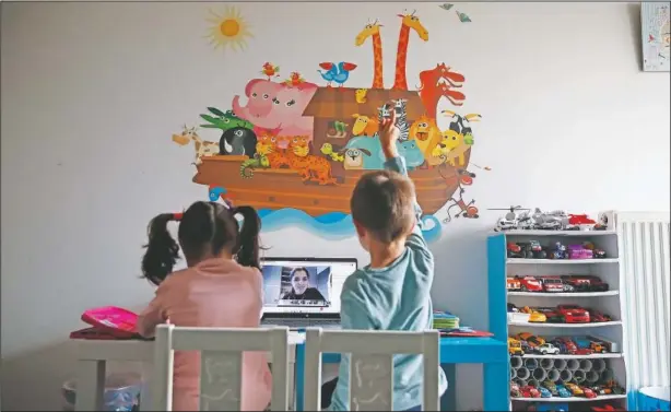  ?? (AP/Thanassis Stavrakis) ?? A kindergart­en teacher reads a fairy story as Panos raises his hand with twin sister Marina during an online lesson in Athens.