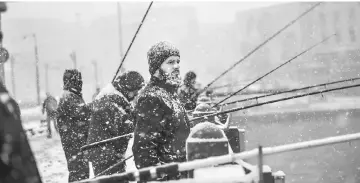  ??  ?? Fisherman fish on the Galata bridge during snowfalls in Istanbul. — AFP photo