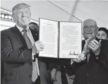  ?? Mandel Ngan / Getty Images ?? President Donald Trump holds up an executive order to streamline the approval process for GMO crops, as Secretary of Agricultur­e Sonny Perdue applauds.