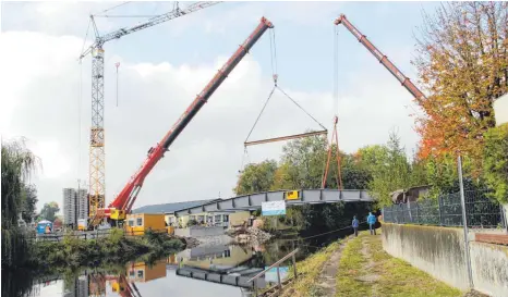  ?? FOTO: MARION BUCK ?? Mit zwei Autokranen wird die neue Holzbrücke gegen Mittag über die Donau gesetzt.