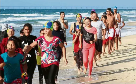  ?? — AFP ?? Hope in troubled waters: The swim team running on the beach during a training session in Beit Lahia.