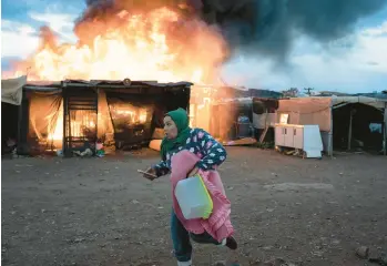  ?? SANTI DONAIRE/AP ?? A woman races past burning shacks during a fire before an eviction by police officers Monday in Almeria, Spain. A migrant camp that was set to be demolished Monday in Nijar, a town in southern Spain, caught fire. More than 400 people live there, many working as temporary laborers in farming estates. Firemen later extinguish­ed the blaze.