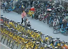  ?? ZHU XINGXIN / CHINA DAILY ?? A woman pushes her child along the road between lines of bikes blocking a sidewalk in Beijing.