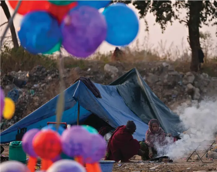  ?? ?? Migrant street vendors selling balloons sit by a bonfire outside their temporary shelter on a cold morning in Jammu, India. Photo: AP/Channi Anand