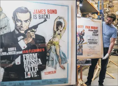  ?? PICTURE: PA ?? STIRRED FOR SALE: Prop Store employee Matt Storey moves posters for James Bond films that due to be sold at auction.