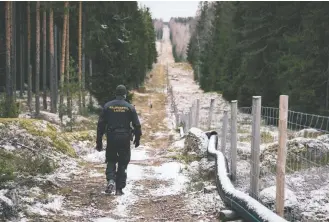  ?? Alessandro Rampazzo/afp/getty Images ?? A border guard walks along a fence near the Pelkola border crossing that marks the boundary between Finland and Russia, in November. Finland plans to build a 124-mile-long border fence with Russia.