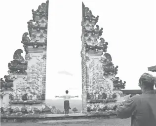  ?? AFP PHOTO ?? THREATENED
A tourist takes a photo at Lempuyang temple as Mount Agung volcano (back L) looms in the background, in Karangasem Regency on Indonesia’s resort island of Bali on December 1, 2017. The volcano’s rumblings in the past week have pounded...