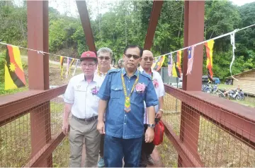  ??  ?? Jamit, accompanie­d by Sigih (front, left), takes a walk along the newly-completed iron bridge crossing Singai Sigih. Behind them (from right) are Ambrose and Watson.