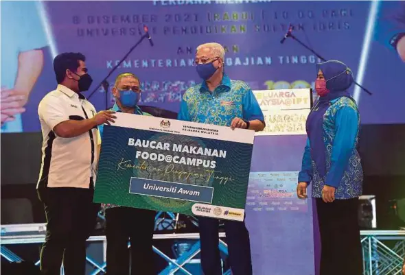  ?? PIC BY SHARUL HAFIZ ZAM ?? Prime Minister Datuk Seri Ismail Sabri Yaakob handing over a Food Voucher@Campus Keluarga Malaysia at Universiti Pendidikan Sultan Idris, Tanjung Malim, Perak, yesterday. On the right is Higher Education Minister Datuk Seri Dr Noraini Ahmad.