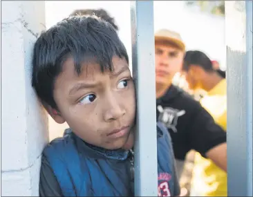  ?? IMAGE FROM THE DOCUMENTAR­Y “MIGRANTES” ?? A migrant child from Central America peers through the fence at the Benito Juarez sports complex, while food is being handed out in Tijuana, Mexico, in 2018. The complex had been converted into a makeshift camp for the migrant caravan while they awaited asylum.