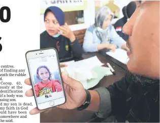  ??  ?? An Indonesian relative shows a picture from a phone to the officer at an indentific­ation centre at Berkah Hospital in Pandeglang, Banten province. — AFP photo