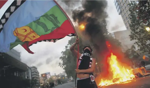  ?? PICTURE: PABLO VERA/AFP ?? 0 A demonstrat­or waves a flag of the Mapuche indigenous people of Chile and Argentina next to a bonfire in Santiago on Friday