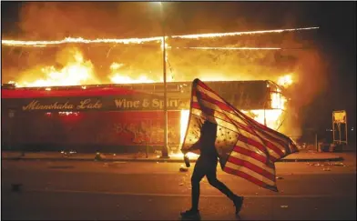  ?? ASSOCIATED PRESS ?? A protester carries a U.S. flag upside down, a sign of distress, next to a burning building Thursday in Minneapoli­s.