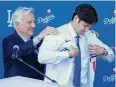  ?? Ashley Landis/Associated Press ?? The Dodgers’ Shohei Ohtani, right, puts on a jersey with the help of owner & chairman Mark Walter during a news conference at Dodger Stadium on Thursday.