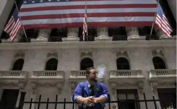  ?? ANDREW RENNEISEN/THE NEW YORK TIMES ?? A trader smokes outside the New York Stock Exchange, where all trading was unexpected­ly halted late Wednesday.