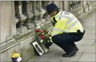  ?? THE ASSOCIATED PRESS ?? A police officer places flowers and a photo of fellow officer Keith Palmer, who was killed in Wednesday’s attack, on Whitehall near the Houses of Parliament in London on Thursday.