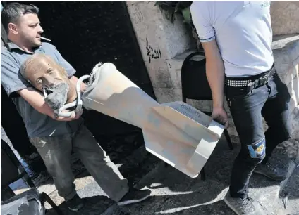  ?? BULENT KILIC/ AFP/ GETTY IMAGES FILES ?? A rebel fighter carries the head of a statue of late Syrian president Hafez al- Assad, along with what appears to be a cluster bomb. Victims of cluster bombs are calling on Canada to ratify the internatio­nal convention to ban the use of these weapons.