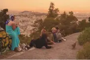  ?? ASSOCIATED PRESS ?? Tourists play with a cat at Lycabettus hill in Athens, with the Acropolis in the background, on Tuesday. The city took on Martian hues as stifling dust clouds, blown across the Mediterran­ean Sea from North Africa, engulfed the Greek capital.