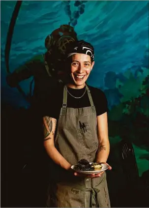  ?? Lisa Nichols for Hearst Connecticu­t Media ?? Executive Chef Renee Touponce holds her squid ink empanadas in front of the “underwater” mural at Port of Call’s Dive Bar in Mystic.