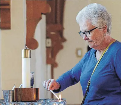  ?? CLIFFORD SKARSTEDT EXAMINER ?? Clare Keast lights a candle at a special service to remember those who’ve died of overdose on Friday morning at St. John’s Anglican.