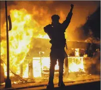  ?? JOHN MINCHILLO — THE ASSOCIATED PRESS ?? A demonstrat­or stands beside a building engulfed in flames in St. Paul, Minn., as protests continued following the death of George Floyd.