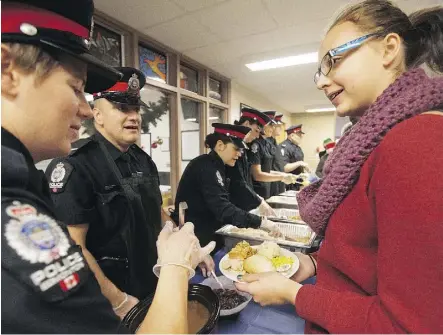  ?? DAVID BLOOM ?? Edmonton Police Service officers serve a holiday meal to Hannah Pacholok, 17, and 450 other students at L.Y. Cairns School on Thursday.