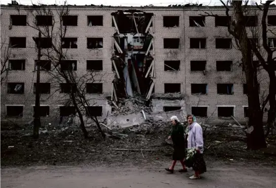  ?? ANATOLII STEPANOV/AFP VIA GETTY IMAGES ?? Two Ukrainian women walked past a hostel destroyed by a Russian missile attack in the town of Selydove, Ukraine, Sunday.