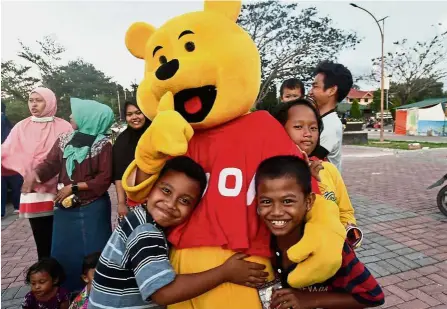  ?? — AFP ?? Much needed cheer: Children hugging a volunteer in a Winnie the Pooh costume as part of a trauma healing programme at a shelter in Palu.