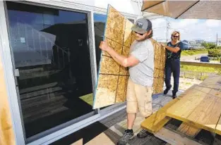  ?? STEW MILNE AP ?? James Masog (front) and Gary Tavares move particle board into place to shore up the sliding glass doors of a client’s house in Charlestow­n, R.I., ahead of Hurricane Henri on Saturday.
