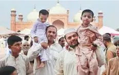  ?? AP ?? Men carry children as they leave the historic Badshahi mosque after offering Eid prayers in Lahore.